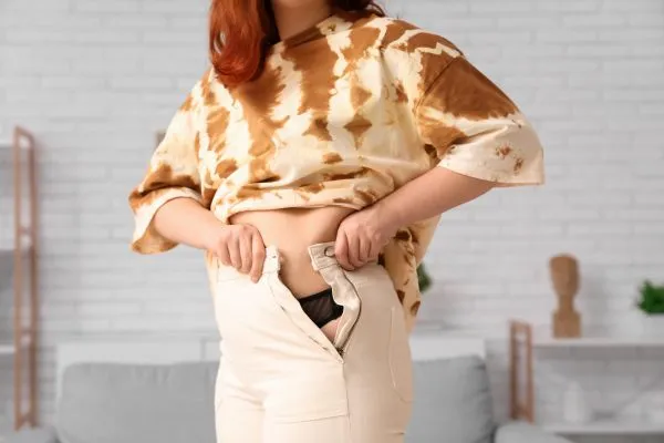 Image of woman trying to do her trousers up after pregnancy weight gain Uttoxeter