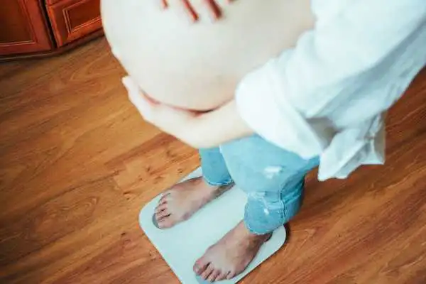 Image of woman weighing herself and experiencing weight gain through pregnancy Uttoxeter